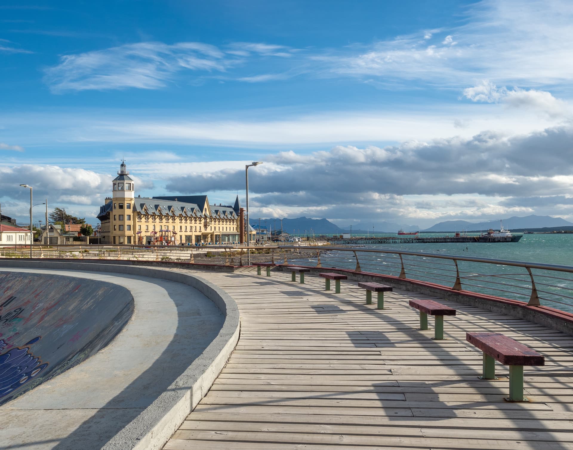 Puerto Natales waterfront boardwalk with yellow hotel, harbor, and mountains in Chilean Patagonia.