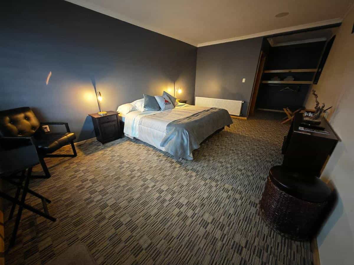 Bedroom with dark blue wall, made bed, leather chair, and patterned carpet in Sheuen-Patagonia.
