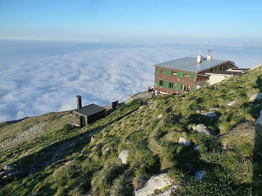 Mountain hut above a sea of clouds on a grassy slope, Prešernova Koča na Stolu.