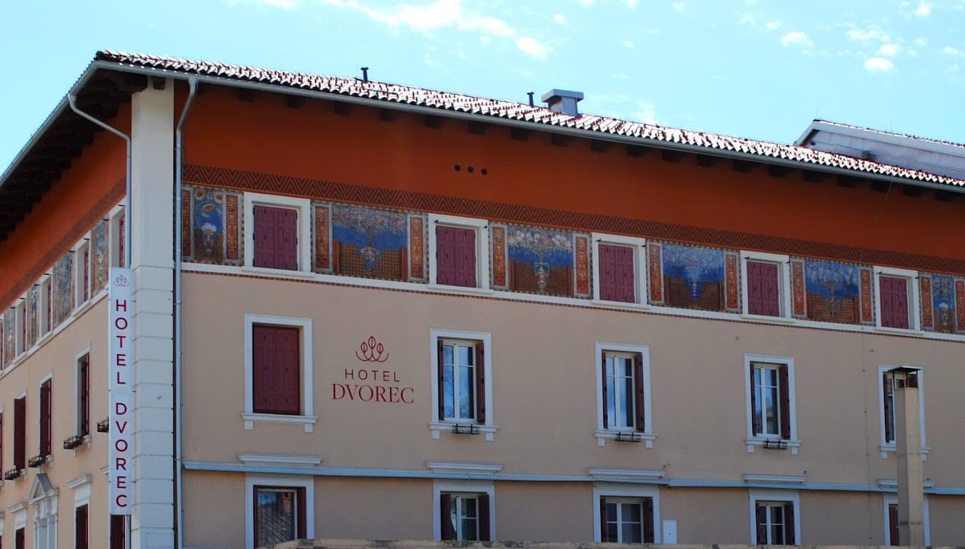 Hotel Dvorec building facade with painted frieze and vertical sign against a blue sky.