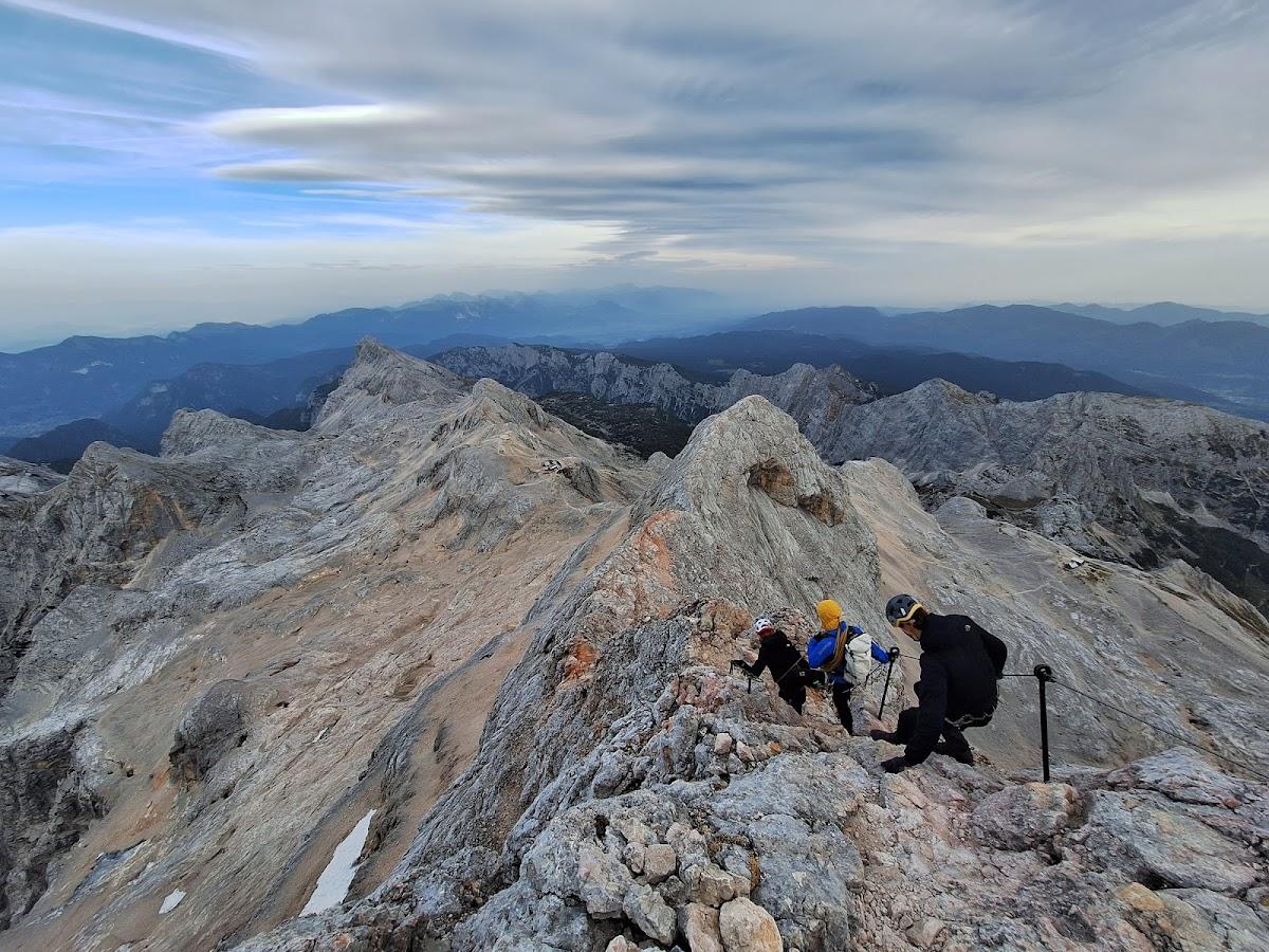 Hikers climbing rocky mountain ridge with exposed peaks and layered blue mountains in background