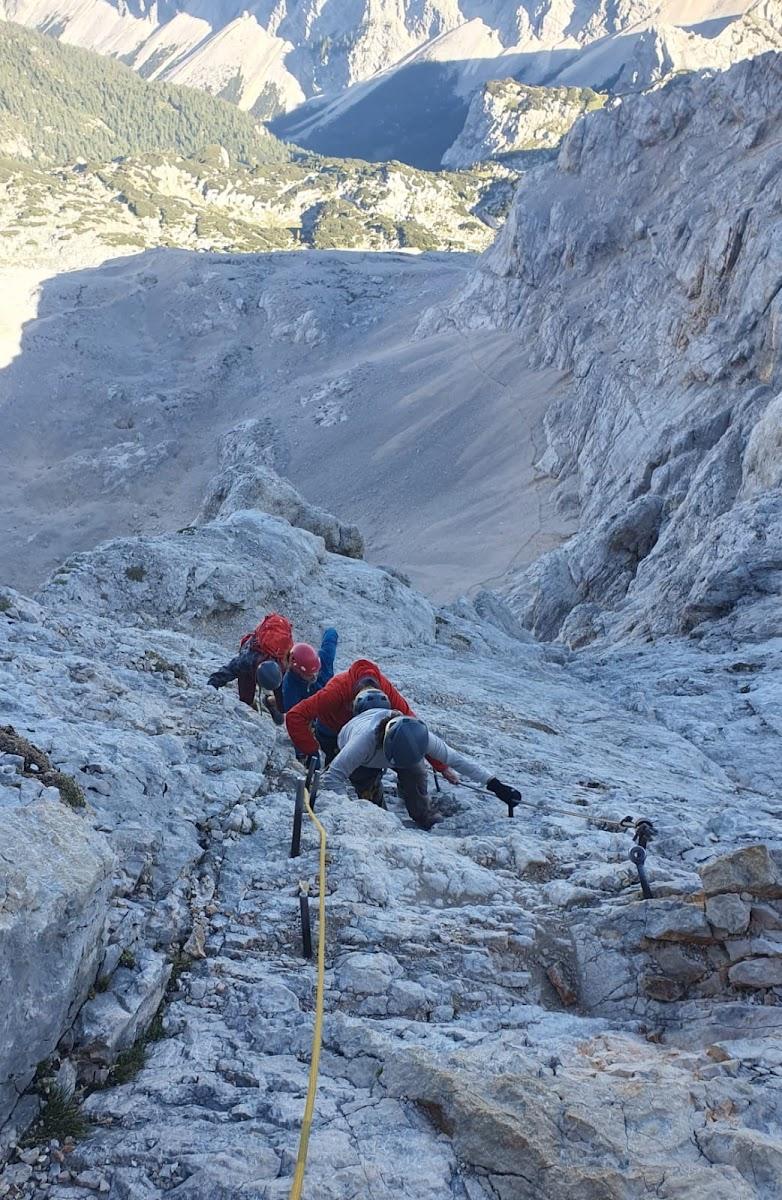 Climbers ascending steep, rocky mountain terrain using fixed cables and ropes.