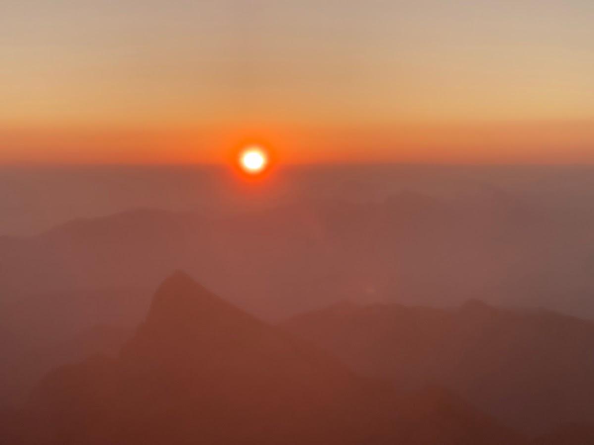 Bright sun setting over hazy, layered mountain ranges at sunrise or sunset