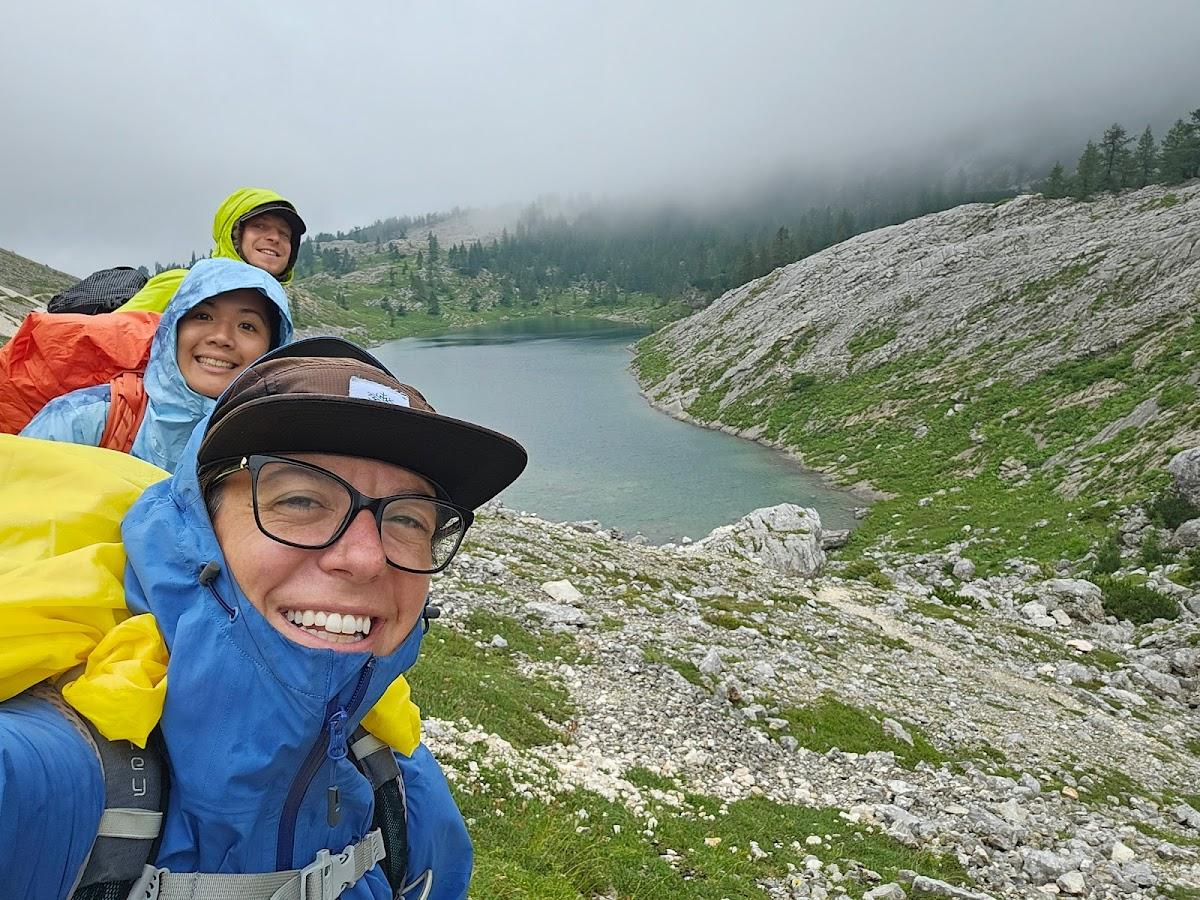 Hikers taking a selfie near a mountain lake with rocky slopes and low clouds
