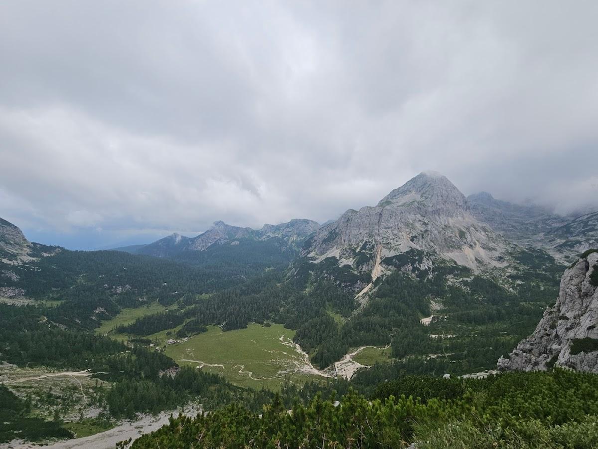 Rugged mountains under cloudy sky overlooking a forested valley with a small clearing.