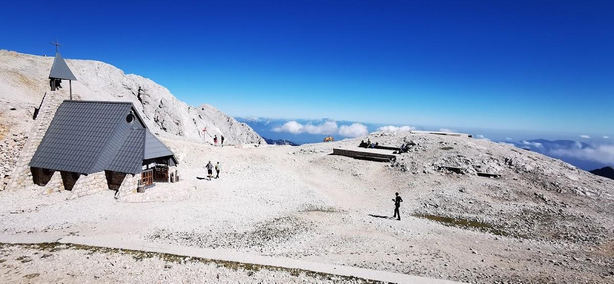Stone mountain chapel with bell tower on rocky summit under clear blue sky