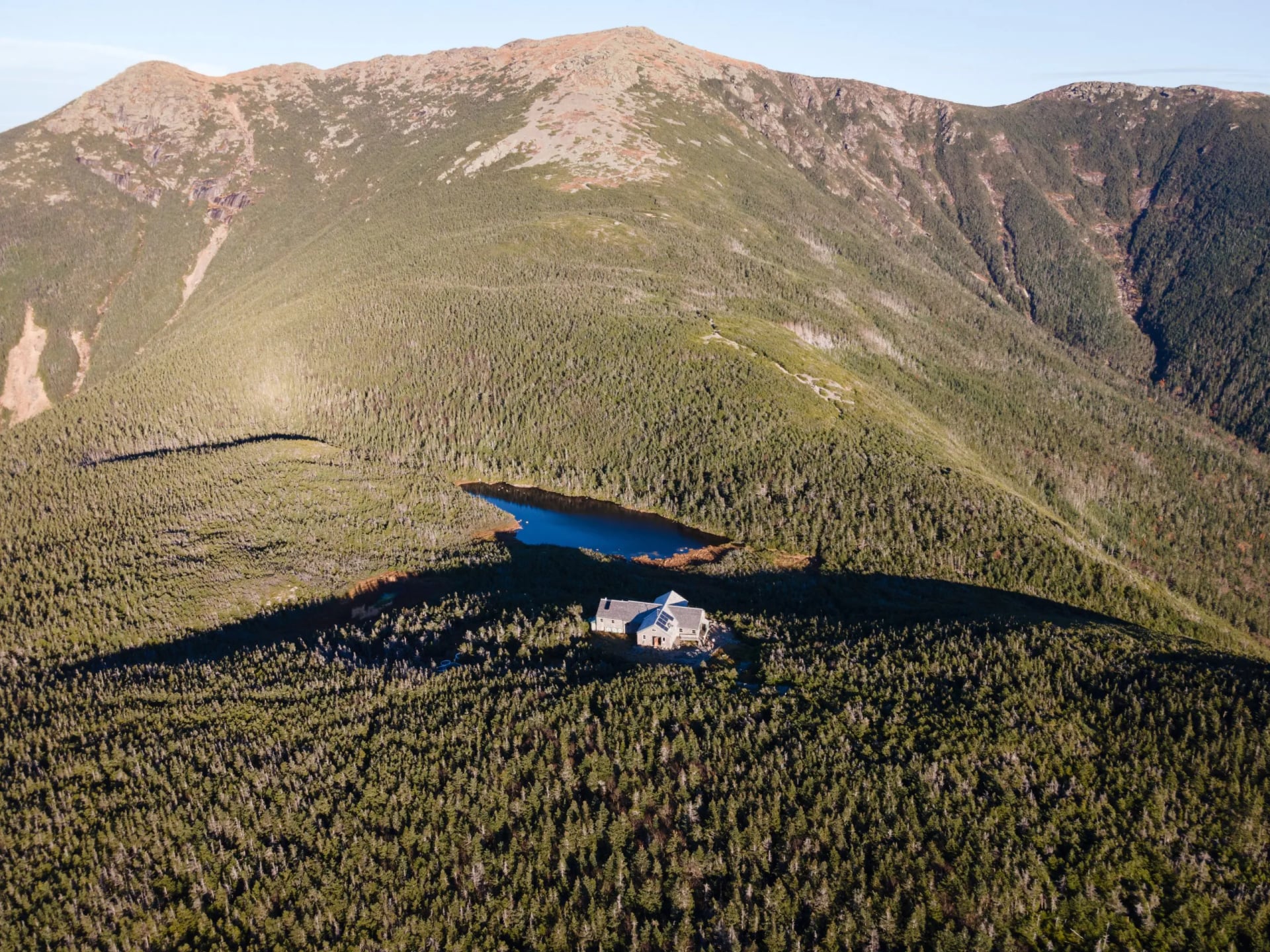 A small hut and a tarn on a green shoulder below a bare summit ridge