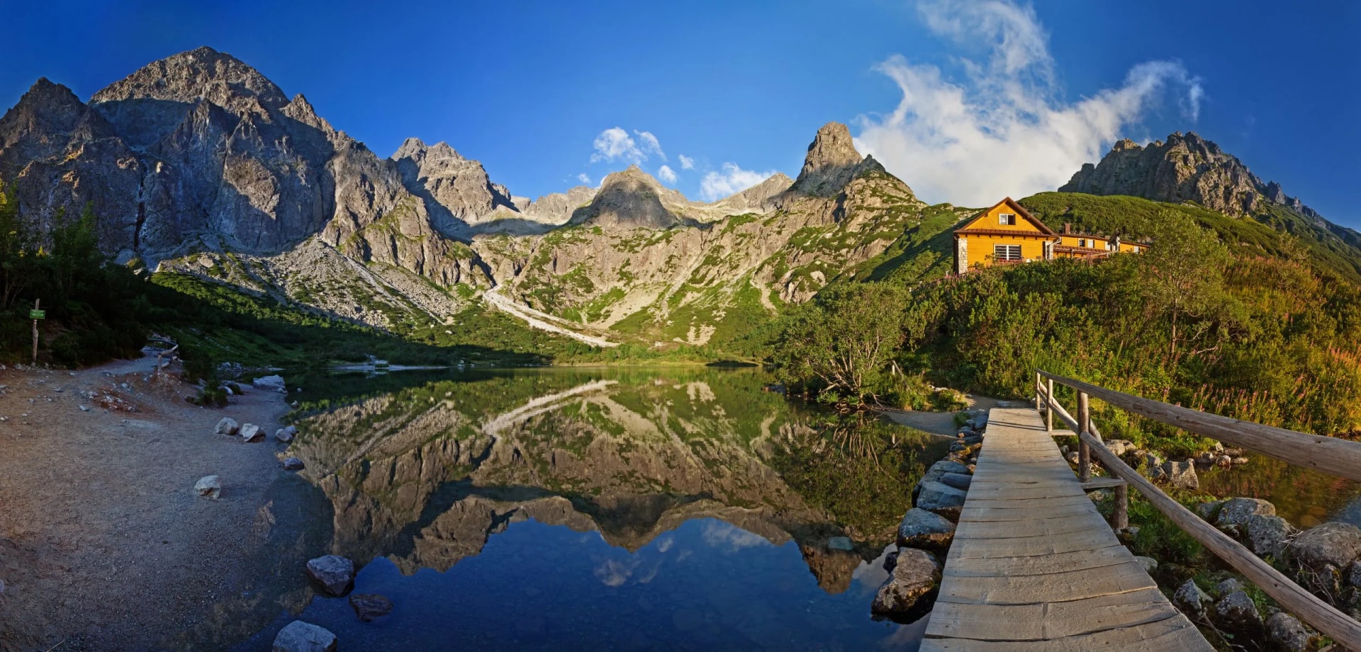 Zelene Pleso Valley Tatras: mountain reflection in lake by yellow mountain hut and wooden boardwalk.