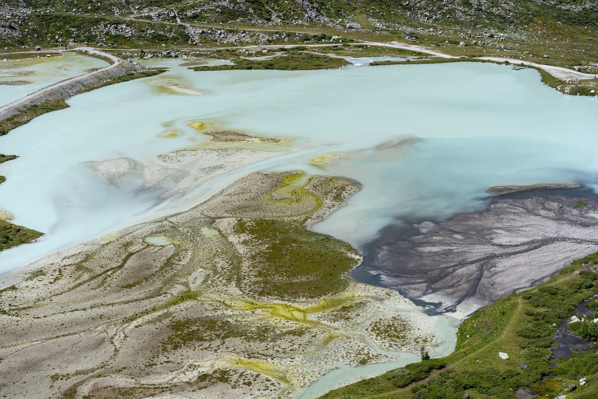 Glacier de Moiry remnants in Switzerland showing milky blue water, sediment deposits, and surrounding green slopes.