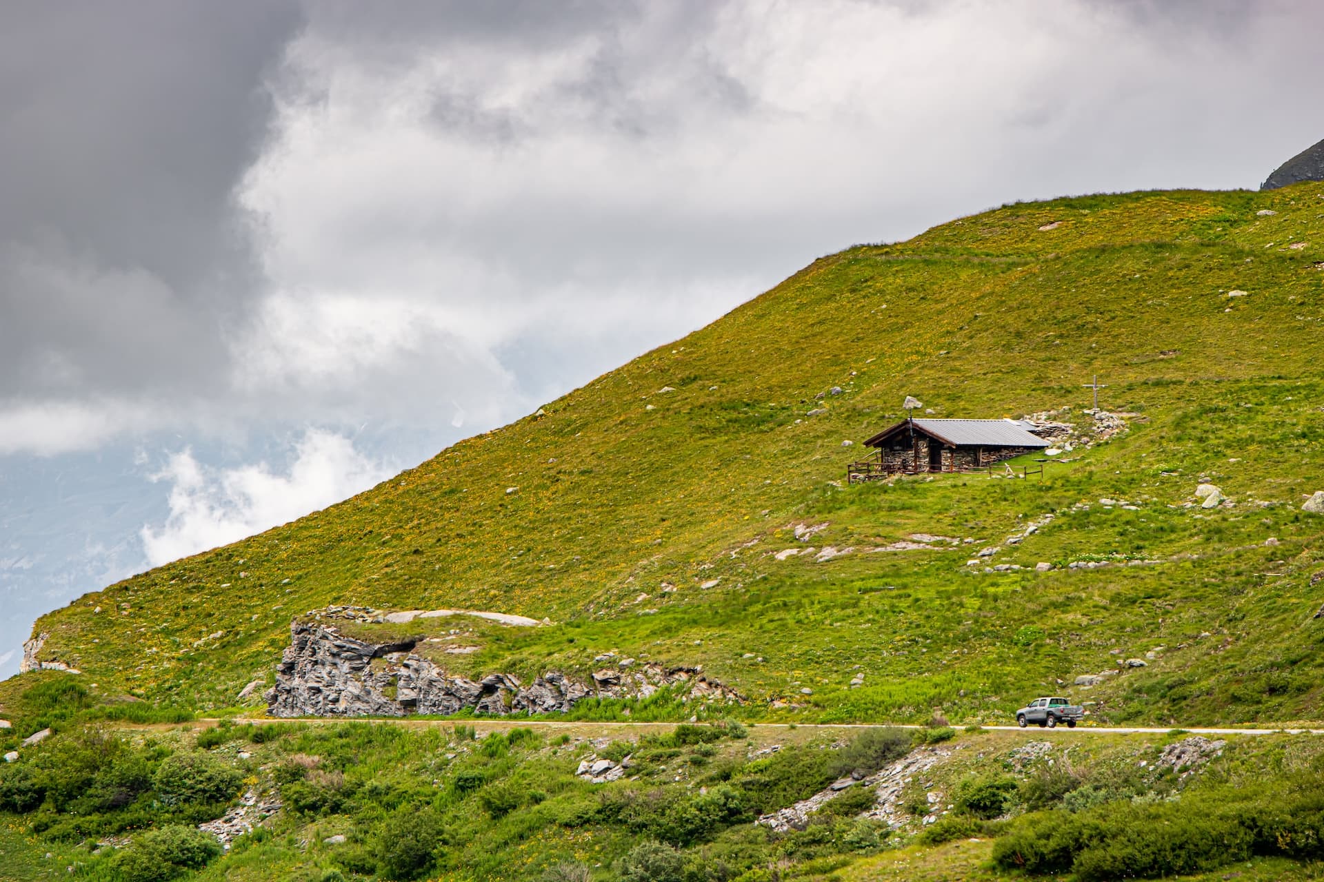 Shepherd hut on steep green alpine slope above road with truck near Lac de Moiry.