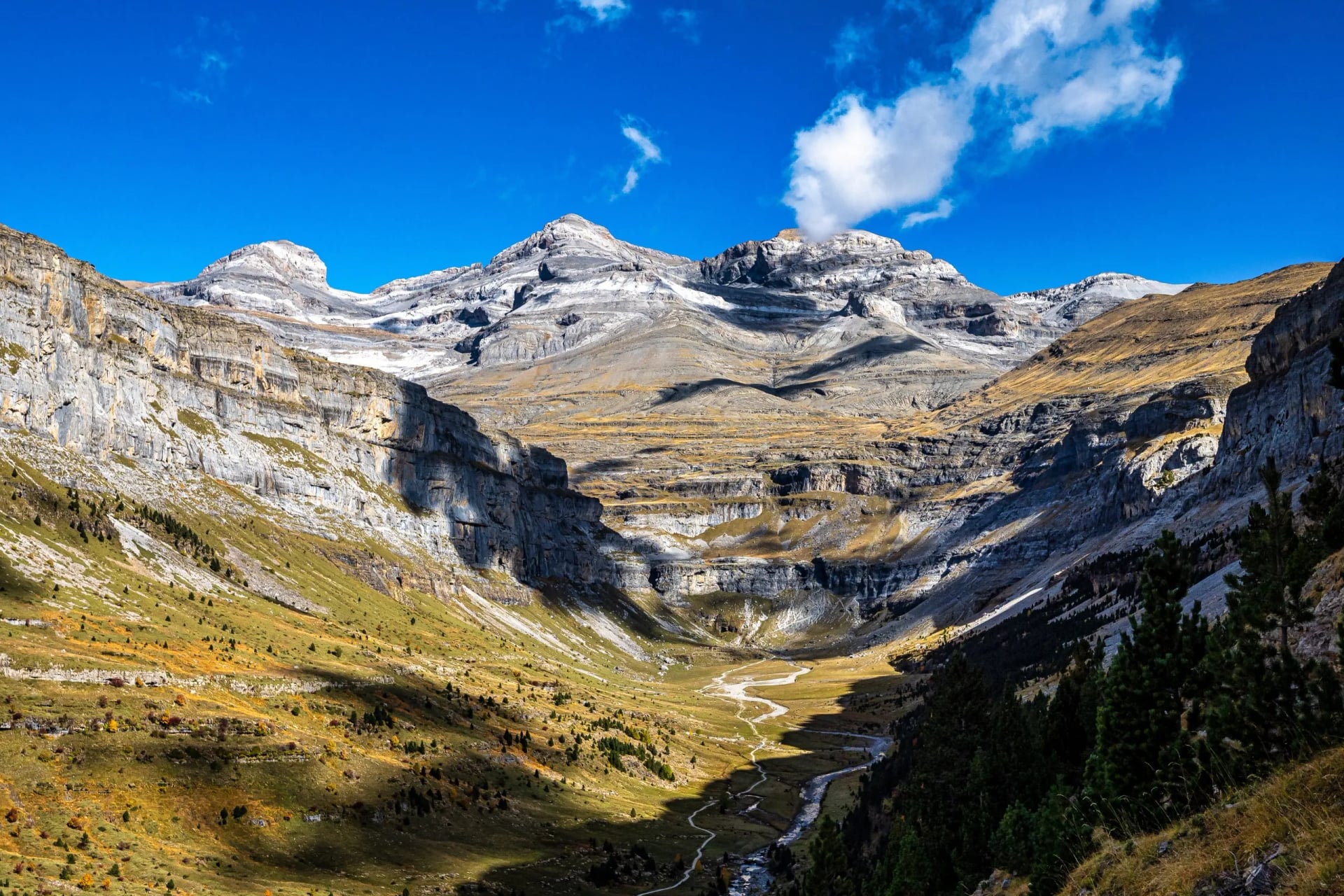 Snow capped limestone cirque above a green valley in Ordesa