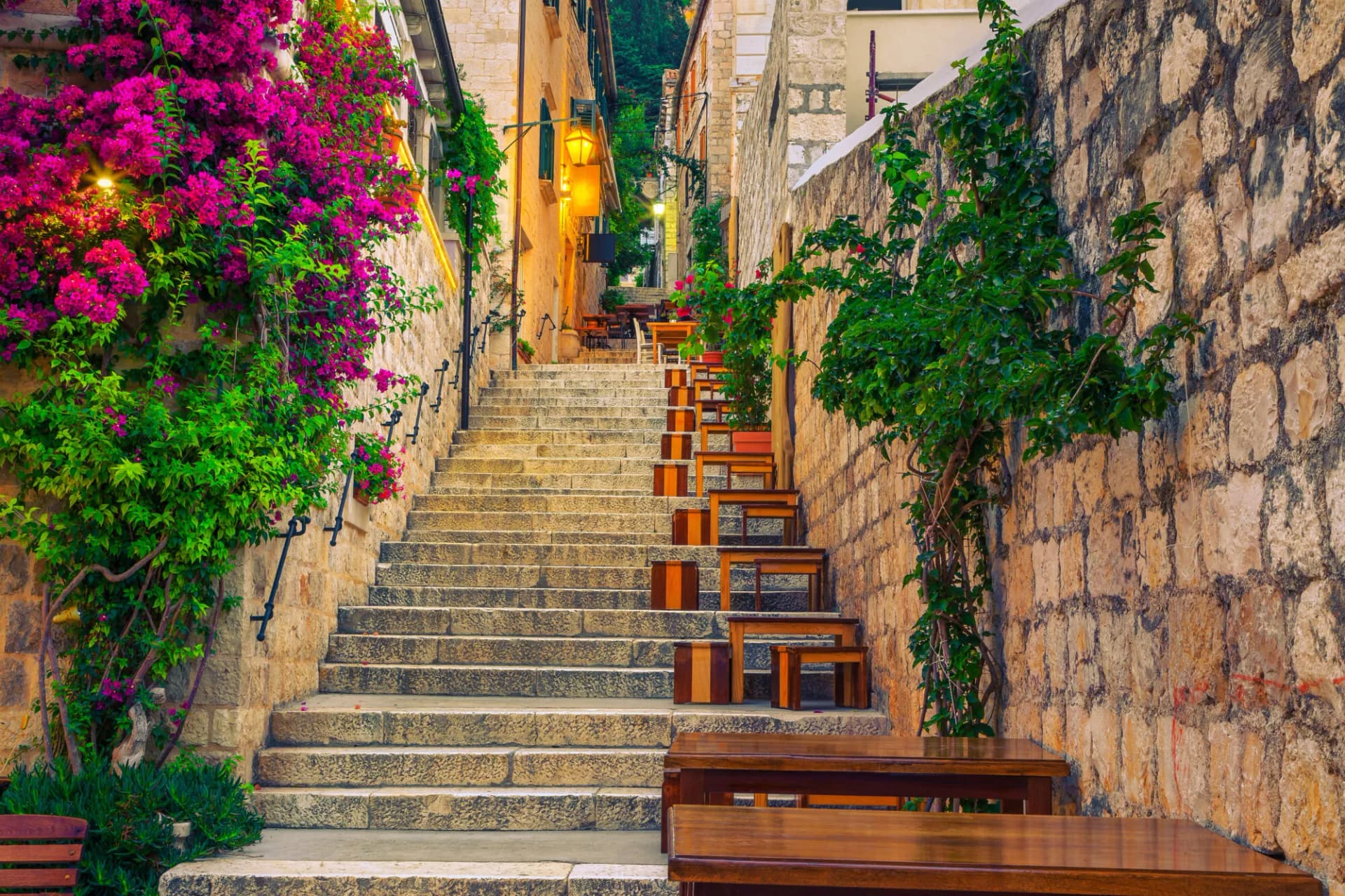 Stone staircase in a narrow alley lined with flowering bougainvillea and outdoor cafe seating in Hvar.