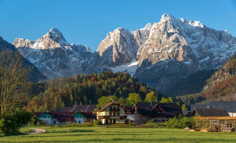 Kranjska Gora village houses below snow-capped Julian Alps mountains at sunrise.