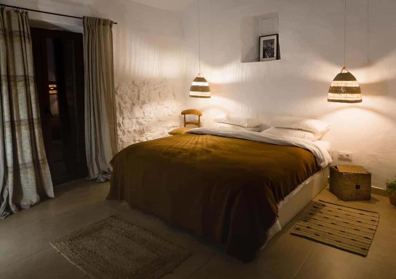 Cozy bedroom with white textured walls, brown bedding, and woven pendant lights in Casa De Los Cuadros