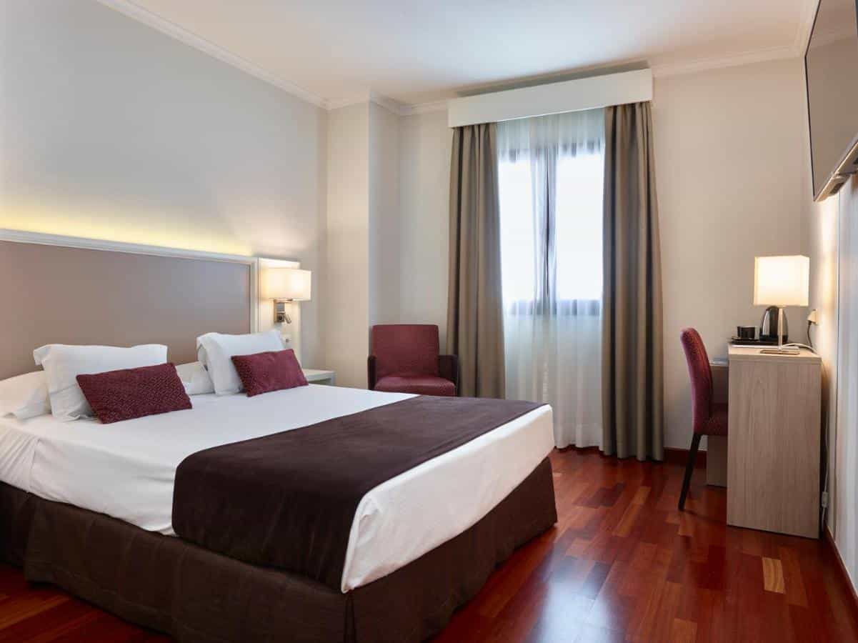 Hotel Maestrana room with large bed, desk, and window with curtains
