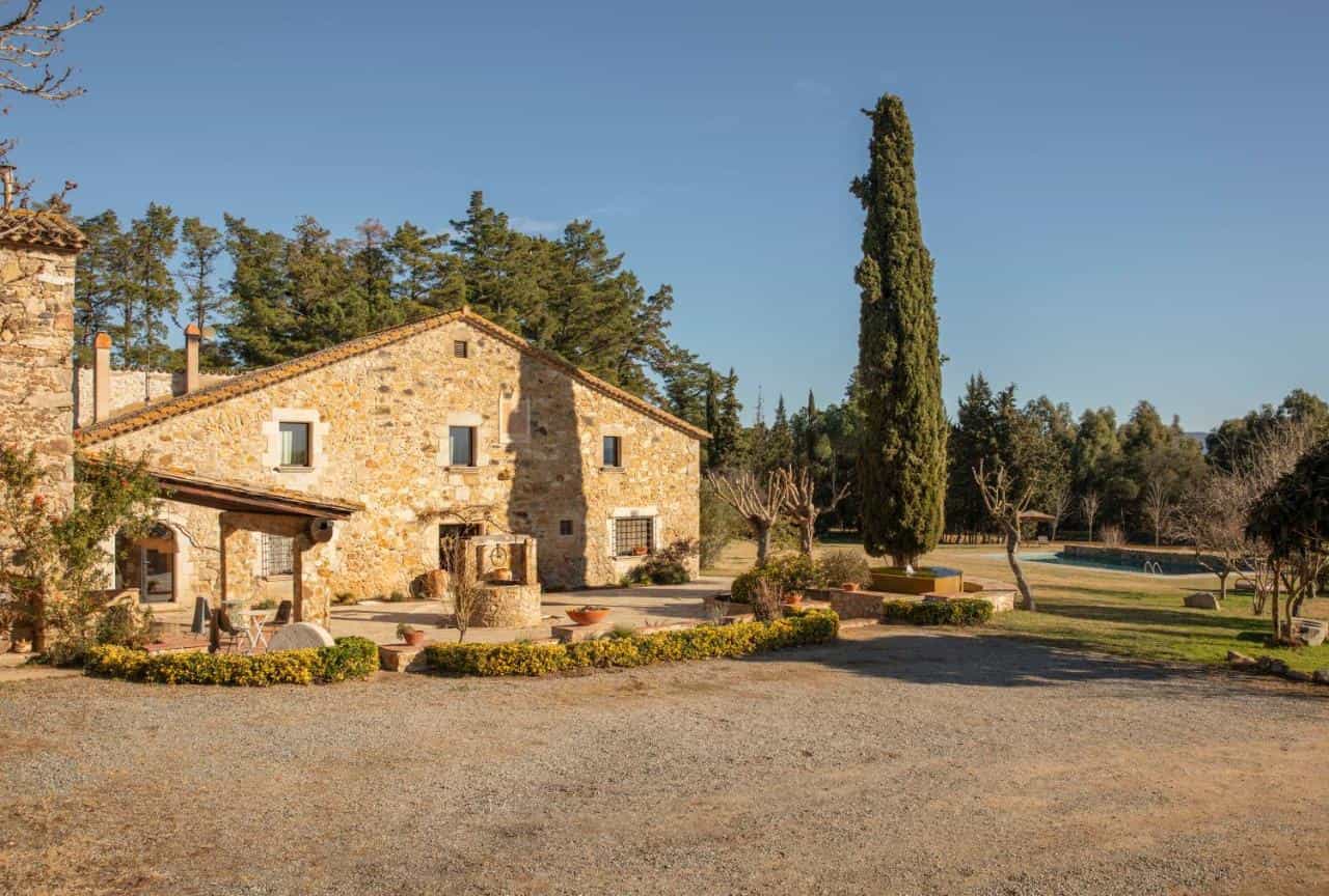 Stone farmhouse with well and tall cypress tree on sunny day near pool