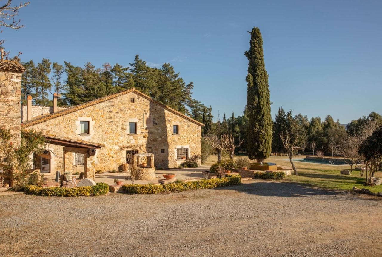 Stone farmhouse with well and tall cypress tree on sunny day near pool