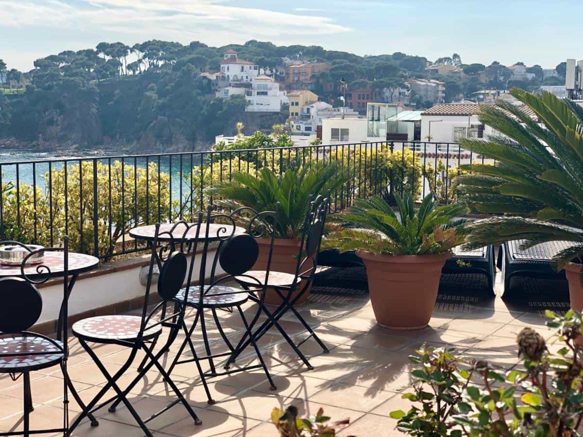 Terrace with wrought iron tables overlooking a coastal town and blue sea, La Muntanya.