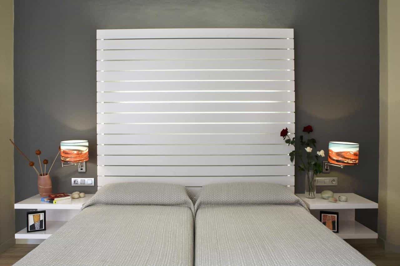 Hotel room with twin beds, white slatted headboard, and wall-mounted lamps with landscape shades.