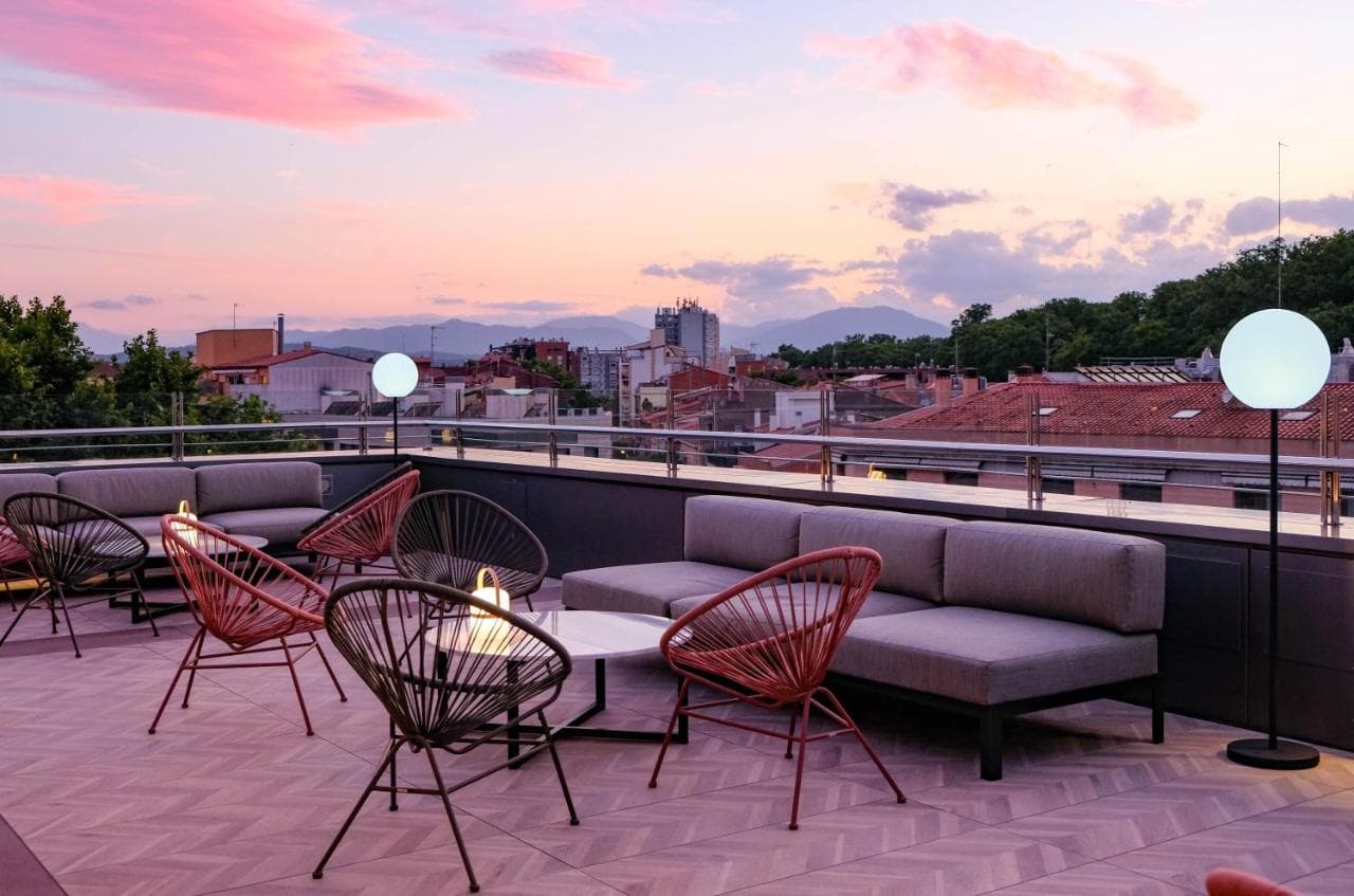 Rooftop terrace lounge with modern seating overlooking city buildings and mountains at sunset.