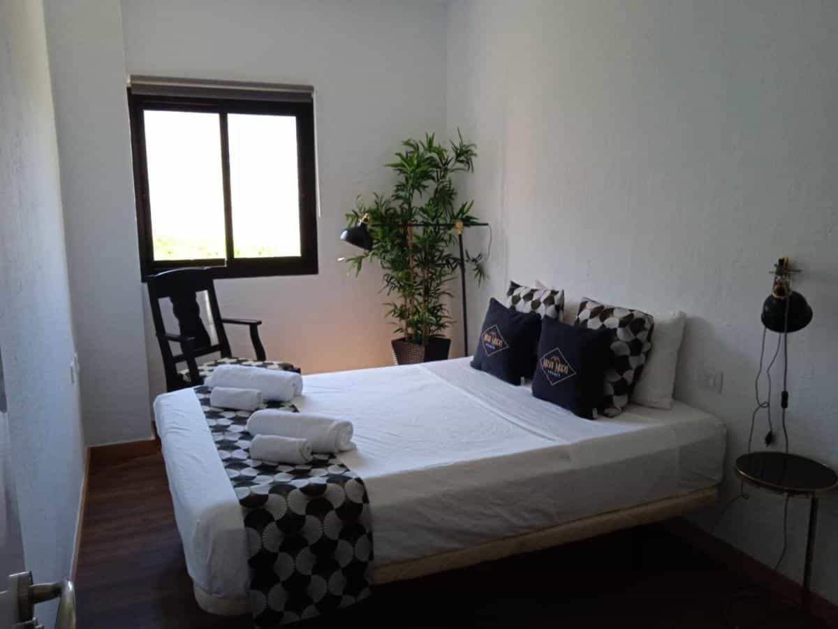 Bedroom with white walls, dark wood floor, and a bed with white linens and patterned runner.