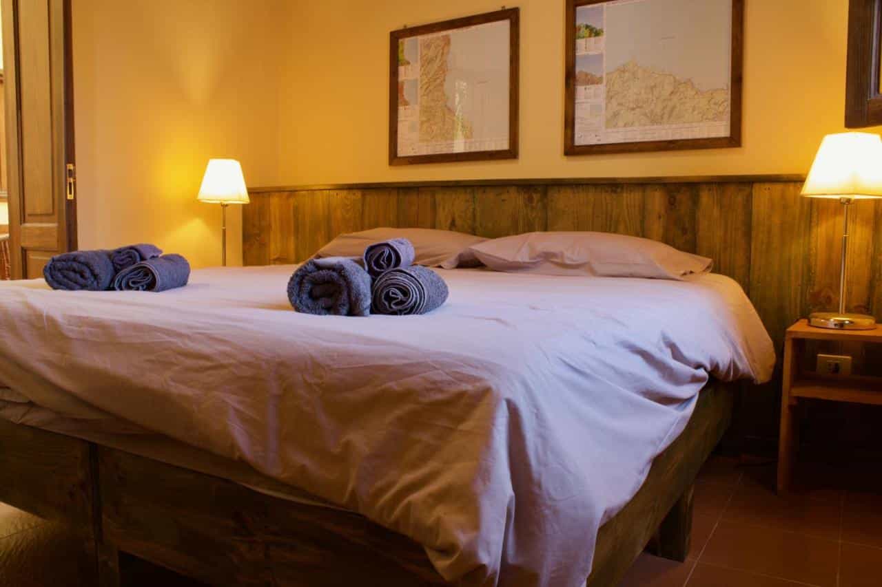 Bedroom with wooden bed frame, maps on wall, and warm lighting at Refugio El Hornillo