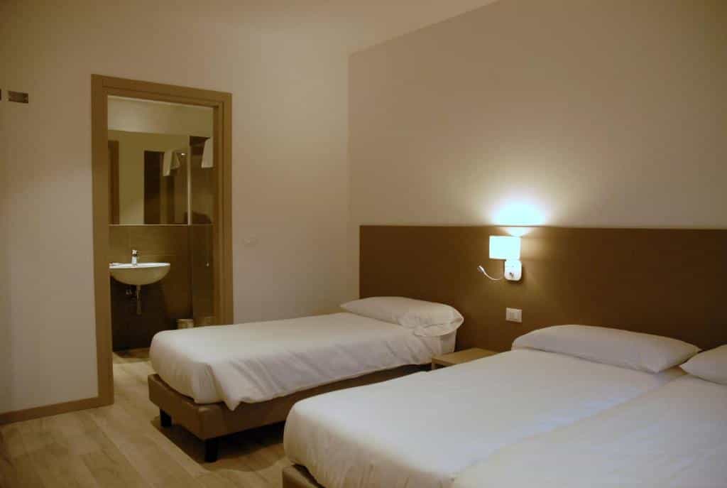 Twin beds in a simple hotel room with an illuminated wall sconce and view of a sink.
