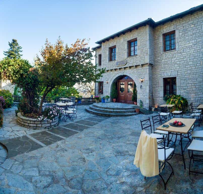 Stone building with outdoor patio seating and trees under a clear blue sky.