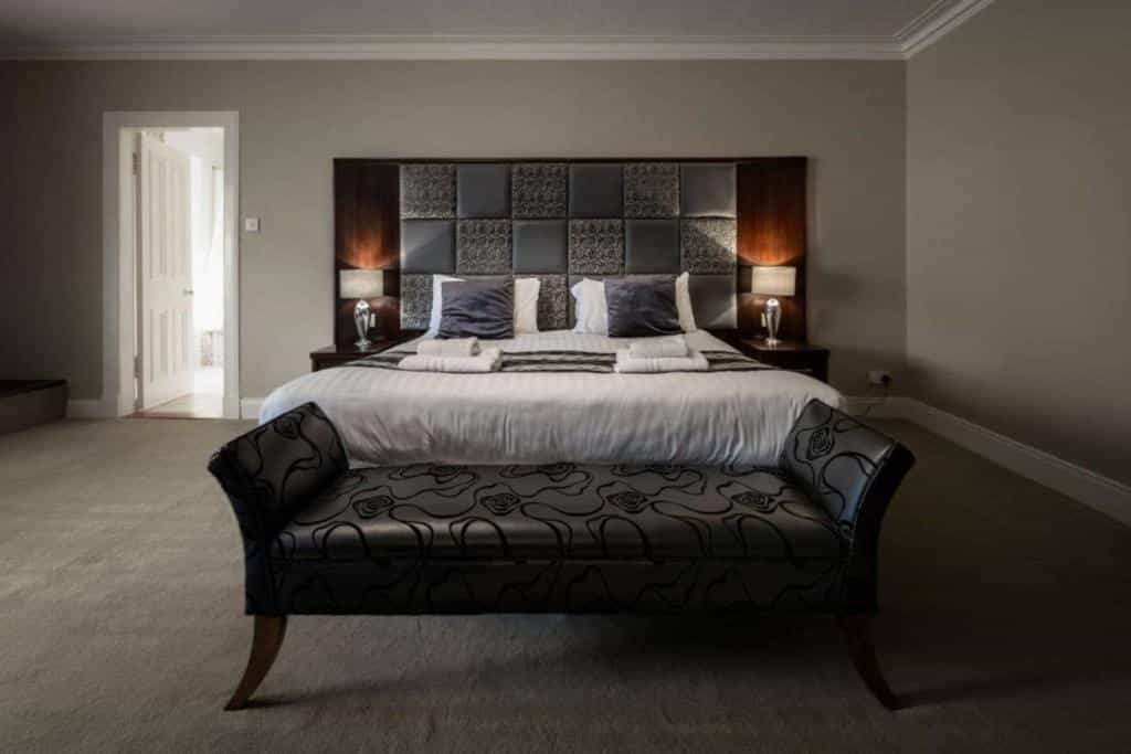 Hotel bedroom with large bed, patterned headboard, bedside lamps, and dark upholstered bench.