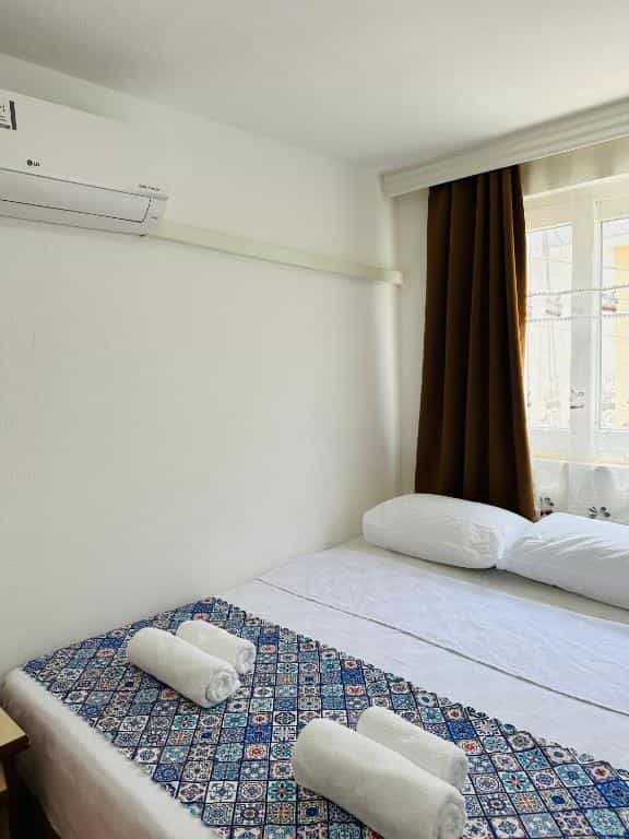 Gelidonya Pansiyon room with white walls, air conditioner, and bed with patterned runner and towels.