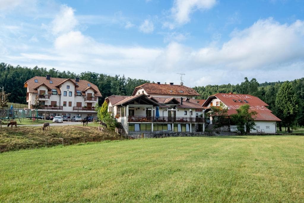 Farm buildings at Kmetija Hudicevec with deer grazing in a grassy field.