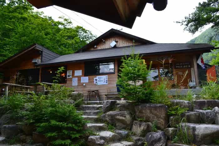 Wooden lodge with stone steps leading up, surrounded by lush green forest, Nakabusa Onsen.