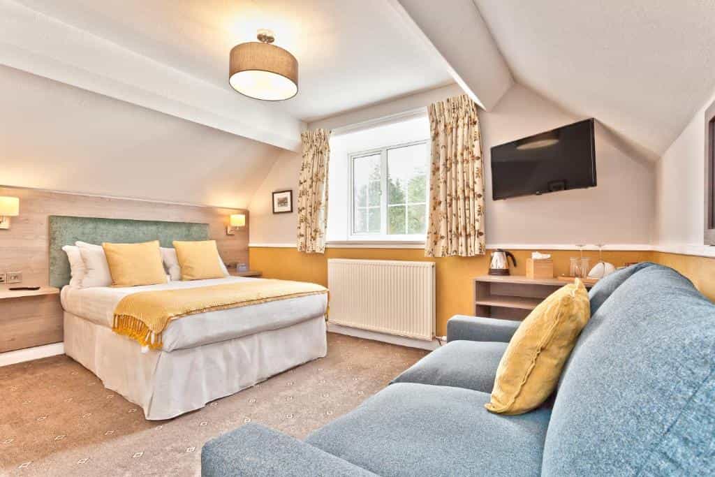 Hotel room with double bed, blue sofa, and wall-mounted TV in The Yewdale Inn, Coniston Village.