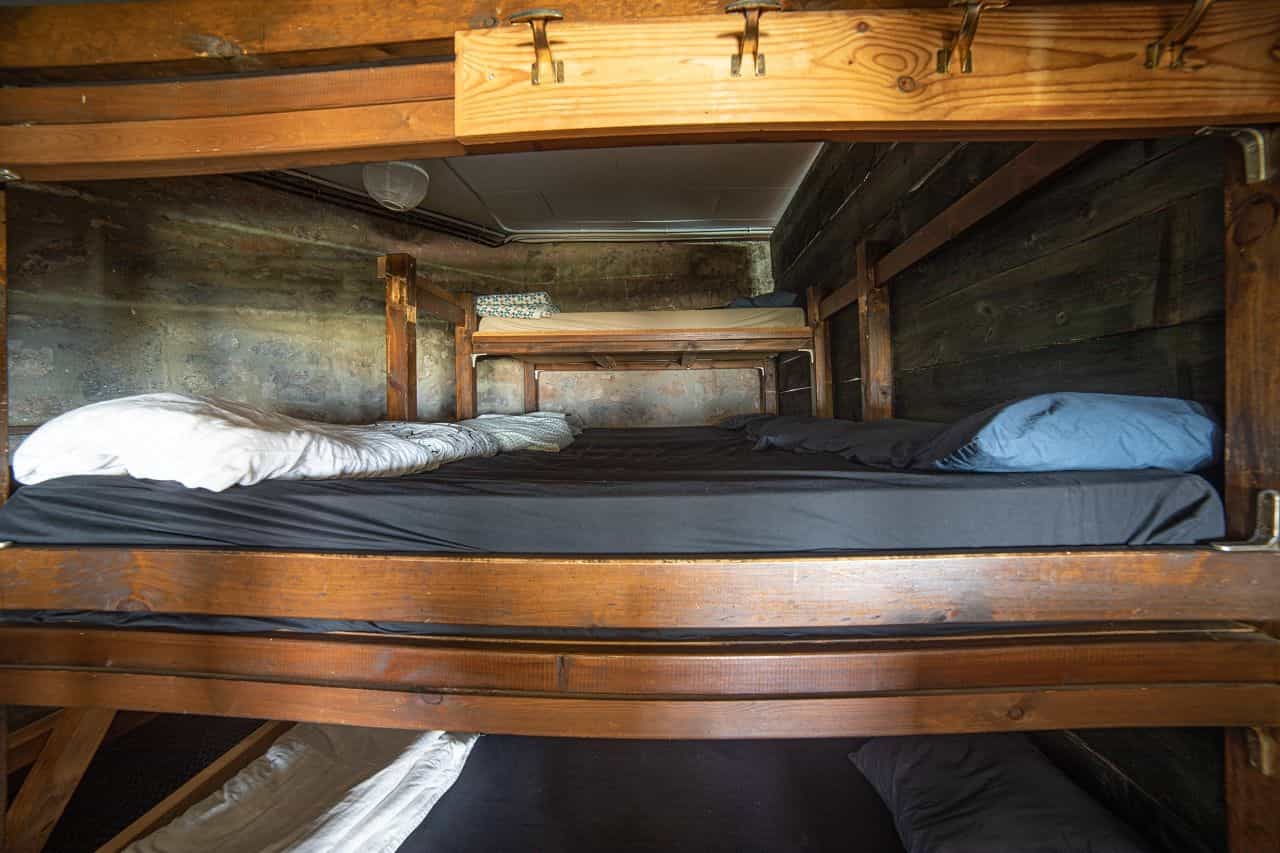 Wooden bunk beds with dark bedding inside a rustic room with stone and wood walls.