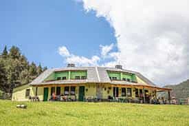 Yellow building with green trim and covered porch in a grassy field under blue sky.