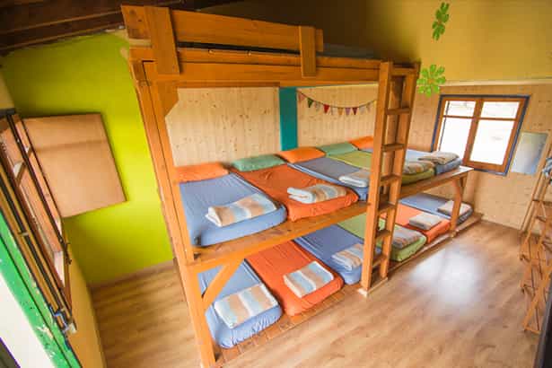Wooden triple bunk beds with colorful bedding in a hostel room with wood paneling