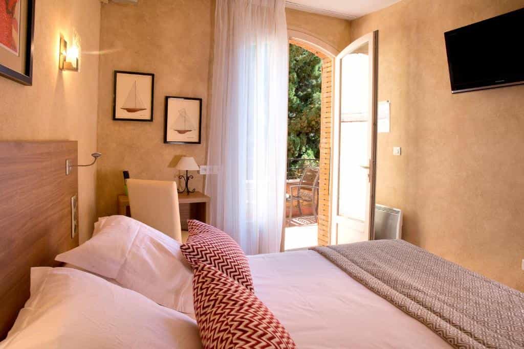 Hotel room with bed, balcony view, and framed sailboat art at Hôtel le Mas des Citronniers.