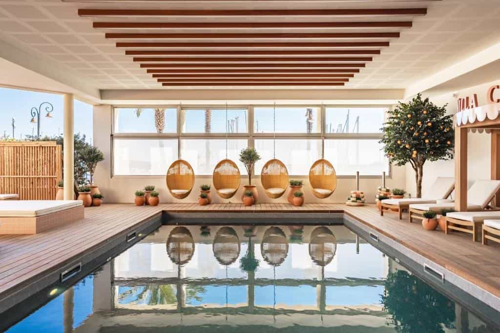 Indoor pool area with wooden deck, hanging wicker chairs, and sun loungers at Villa Camille Hotel & Spa.