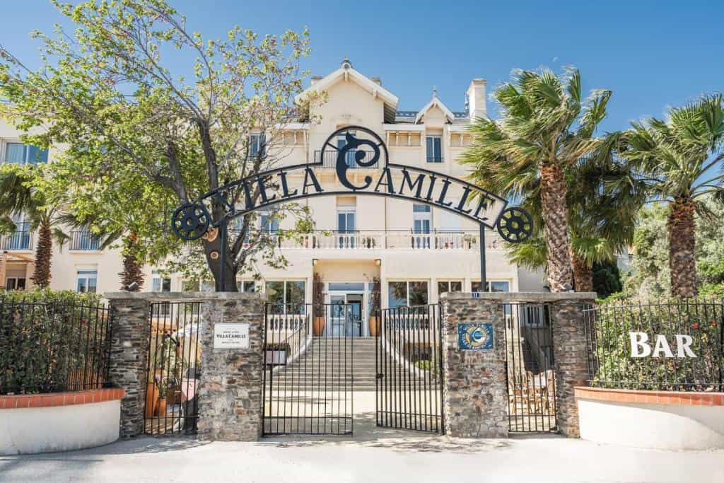 Villa Camille Hotel & Spa entrance with wrought iron sign, stone pillars, and palm trees.