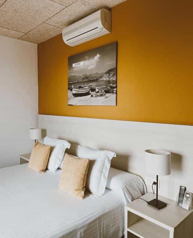 Hotel room with white bedding, yellow accent wall, and black and white boat artwork.