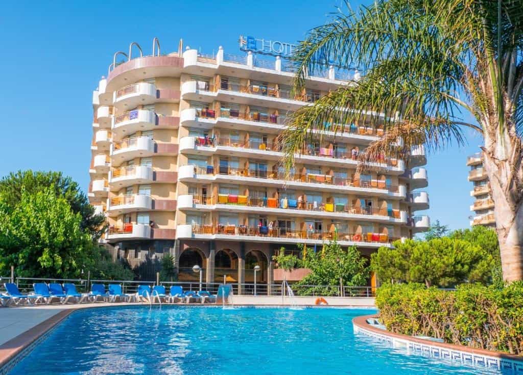 Hotel Blaumar with curved balconies, pool, and palm tree under a clear blue sky.