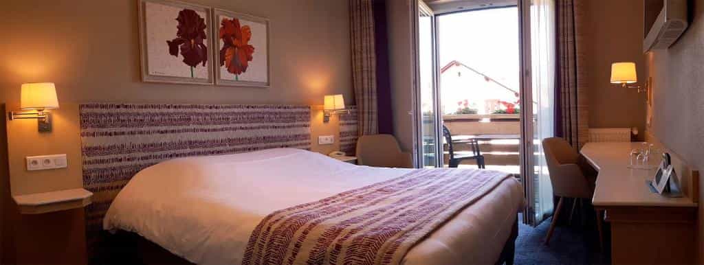 Hotel room with large bed, artwork, and balcony access at Hôtel les Remparts.