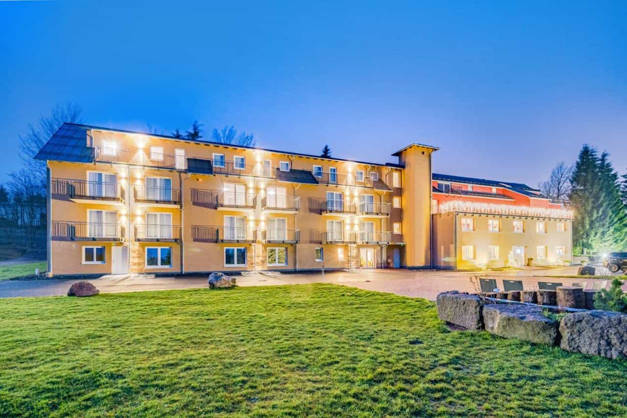 Illuminated multi-story hotel building with balconies and green lawn at dusk
