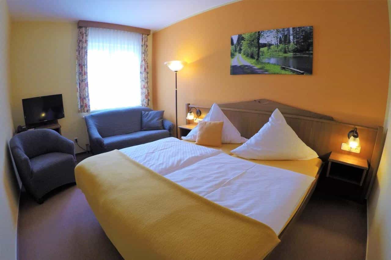 Hotel room with large bed, blue sofa, armchair, and nature artwork on orange wall.