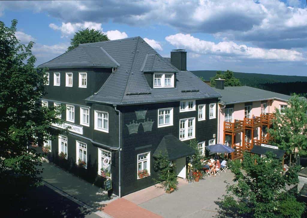 Hotel building with dark slate siding and outdoor dining area surrounded by green hills.