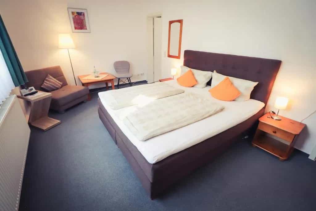Hotel room with large bed, brown headboard, orange pillows, and a small seating area.