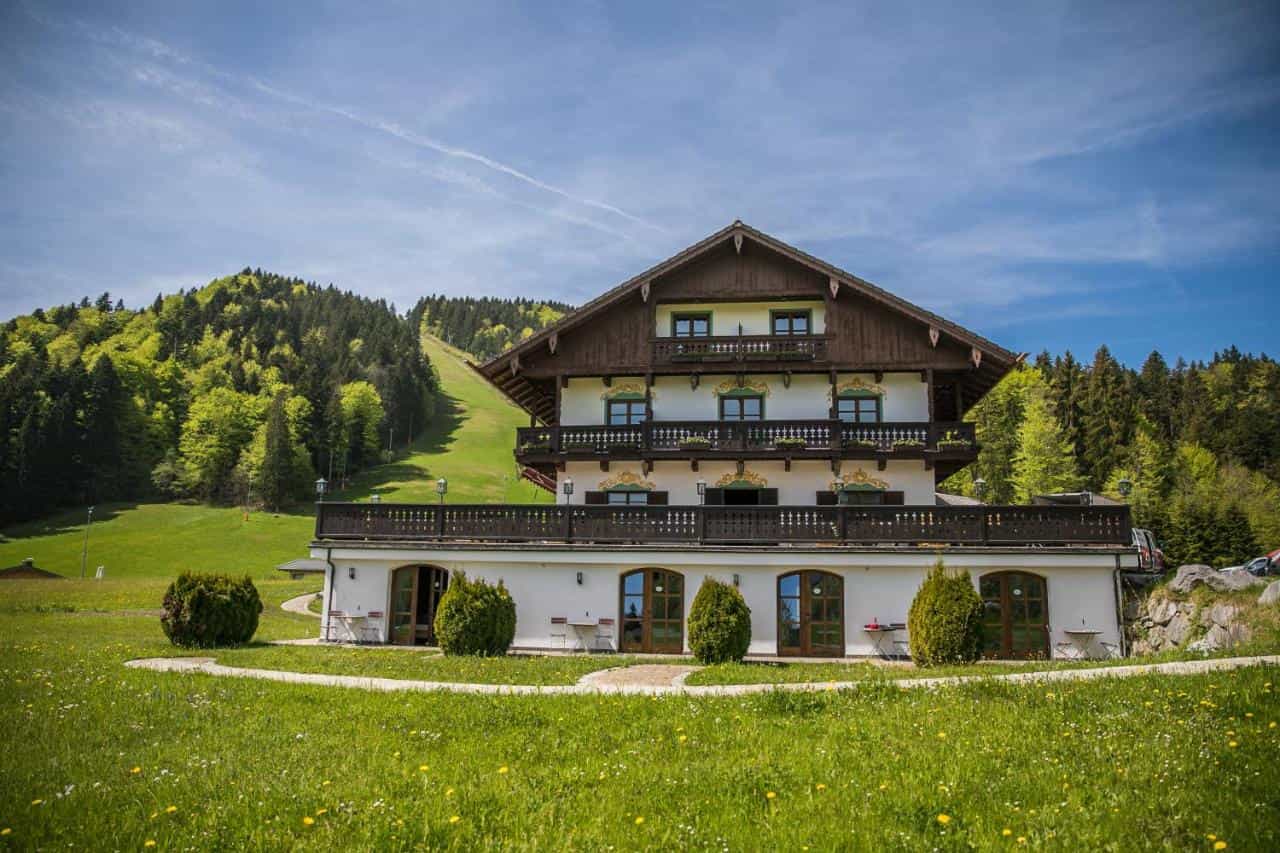 Berghotel Sonnenbichl with balconies, set against a green, forested mountain slope under blue sky.