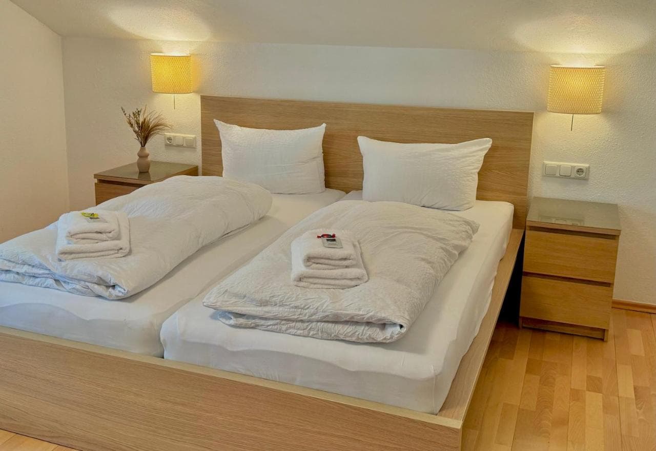 Twin beds with white duvets and pillows, wooden headboard, and bedside lamps in Hotel Königslinde room.