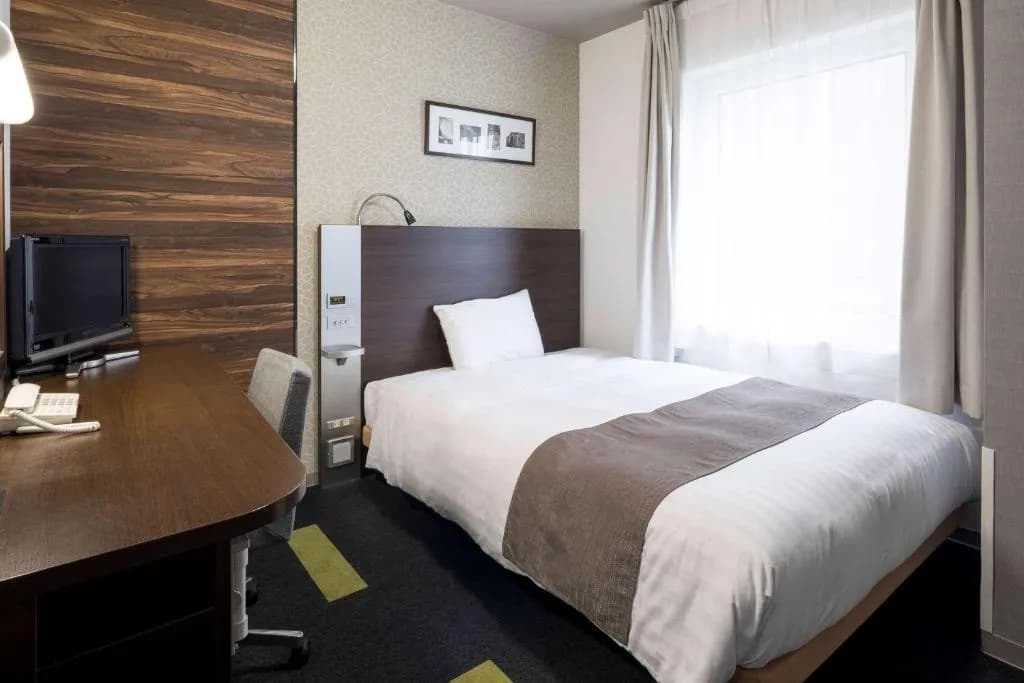 Single hotel room with bed, desk, TV, and bright window in Hotel Higashi-Nihombashi.