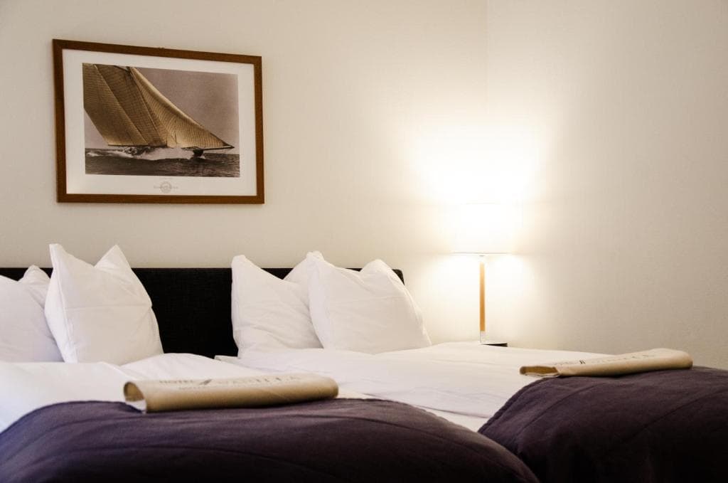 Hotel room with twin beds, white pillows, and framed sailboat artwork above the headboard.
